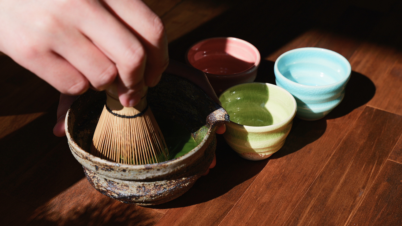 He is whisking the deep green matcha poured into the tea bowl with a tea whisk.